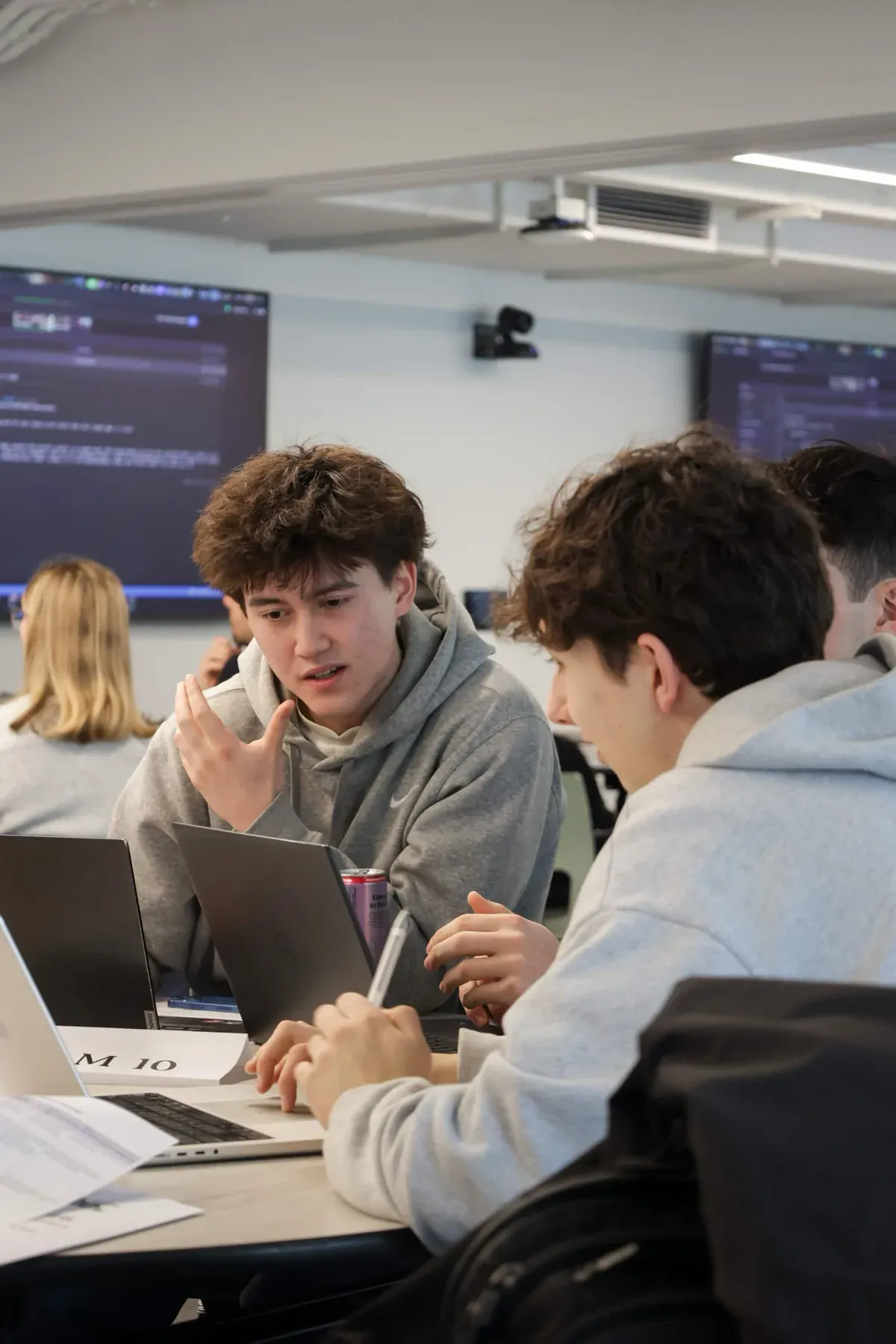 Students collaborating closely around laptops during an AINU build event
